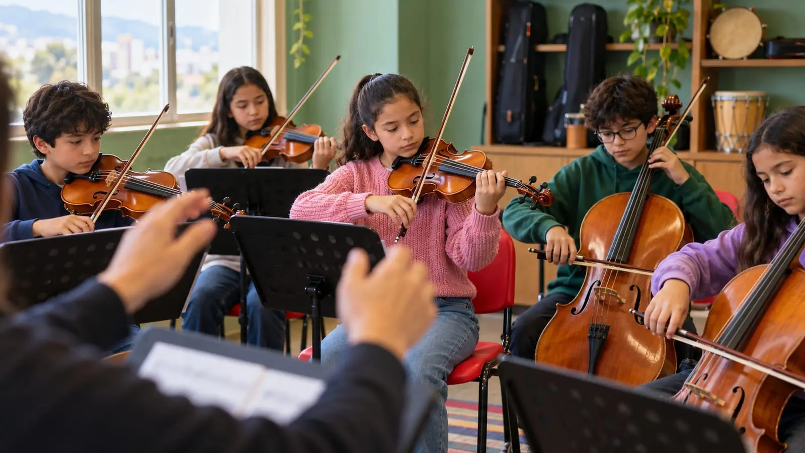 Niña toca el violín sentada en un semicírculo con otros chicos en un salón de clase, con las manos de un director al frente